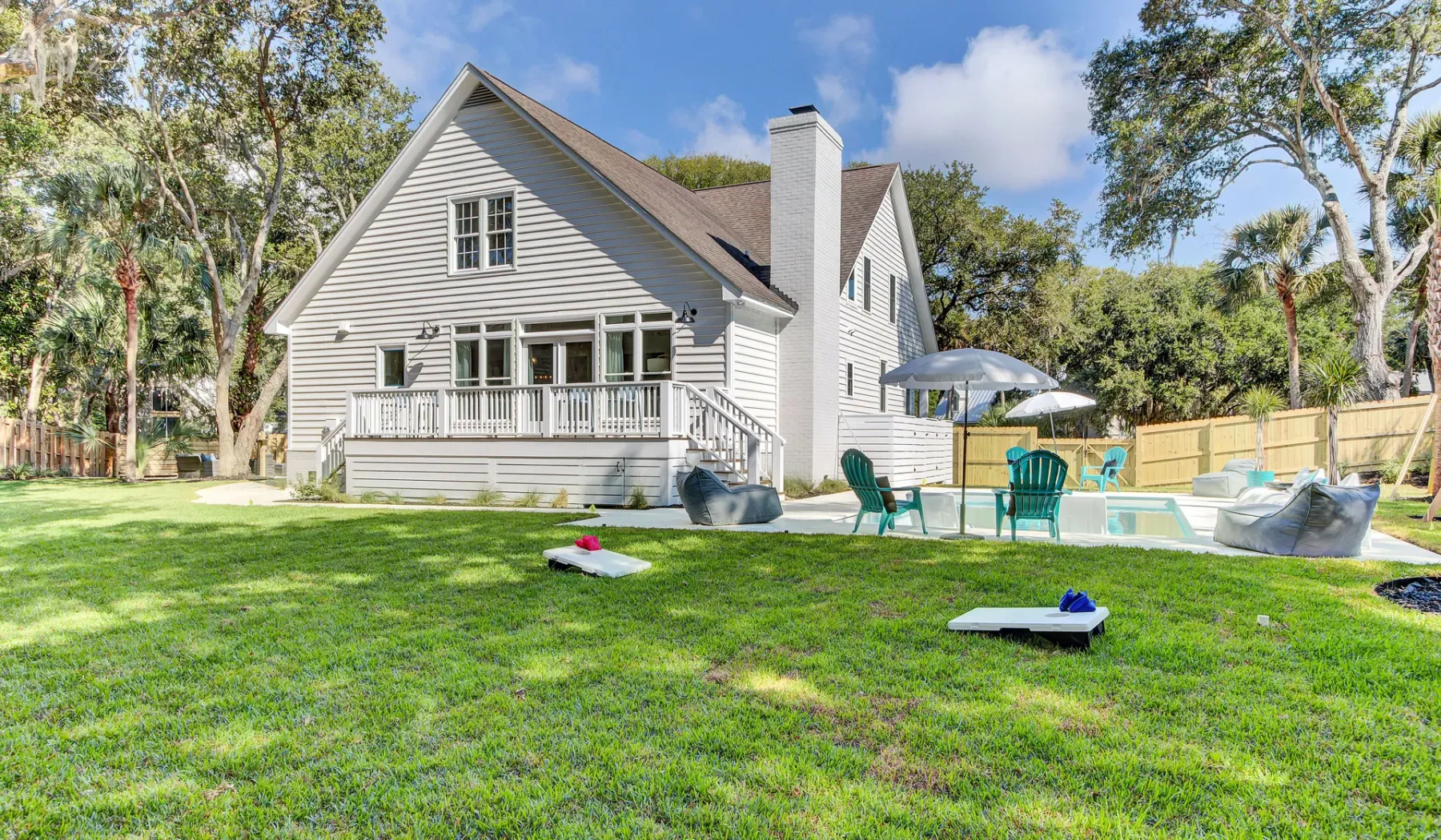 A white house overlooks a grassy backyard with a pool and patio seating.