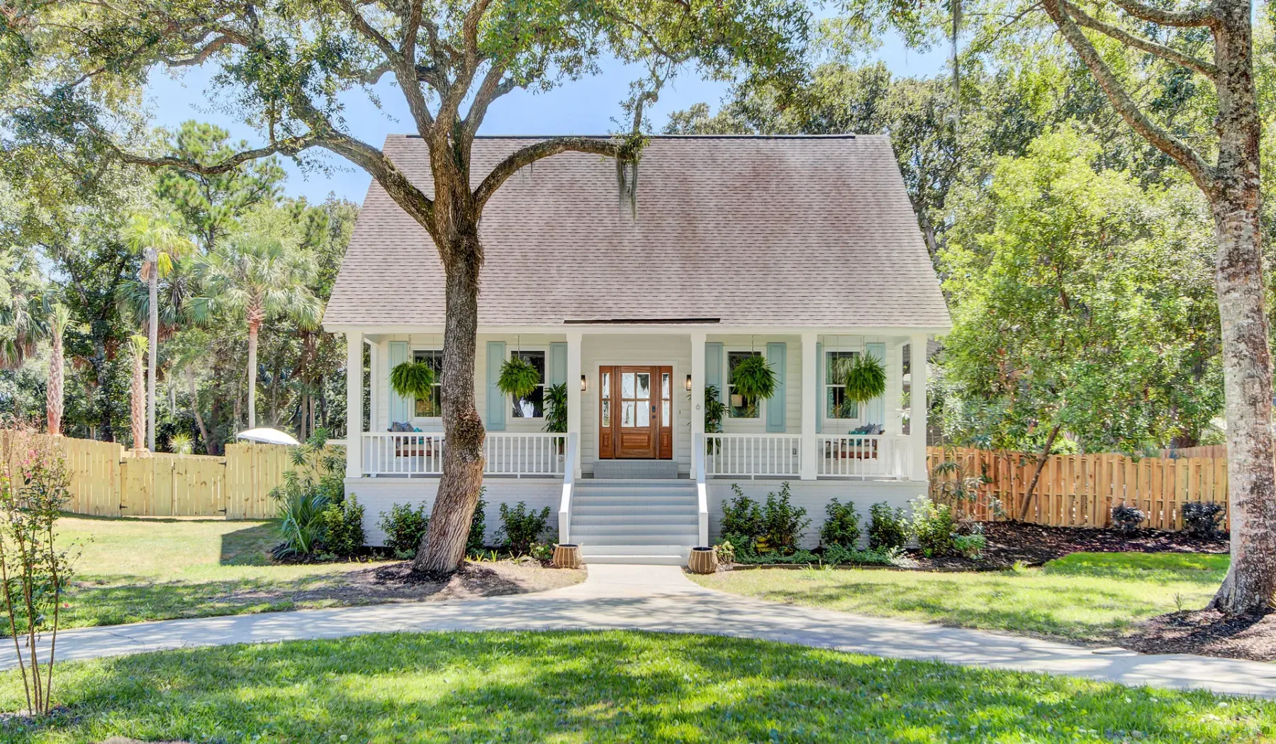 A white house with a broad porch and front steps sits among leafy trees.
