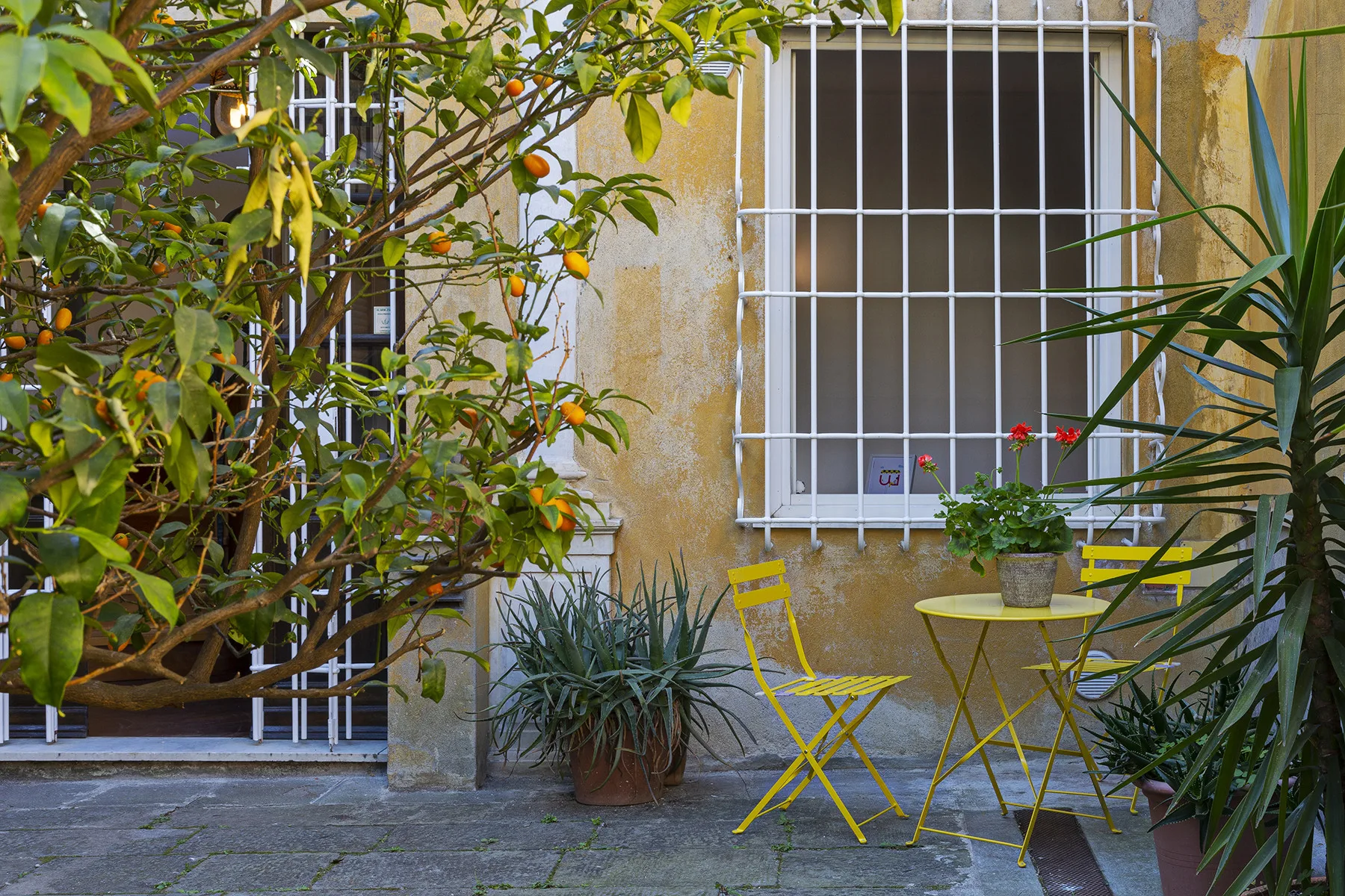 Shared amenity: A courtyard patio with yellow seating and potted plants beside barred windows.