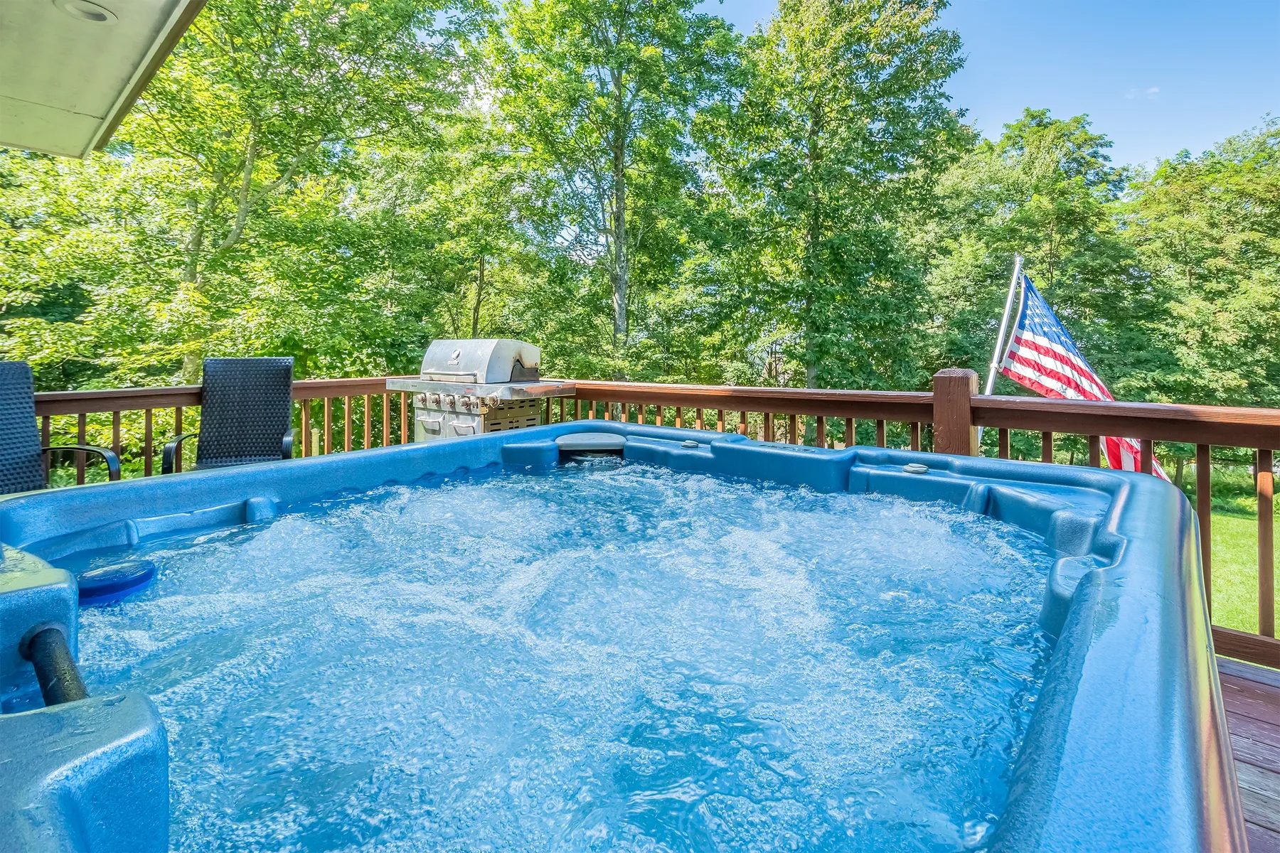 Un jacuzzi al aire libre está en una terraza de madera bajo árboles frondosos.