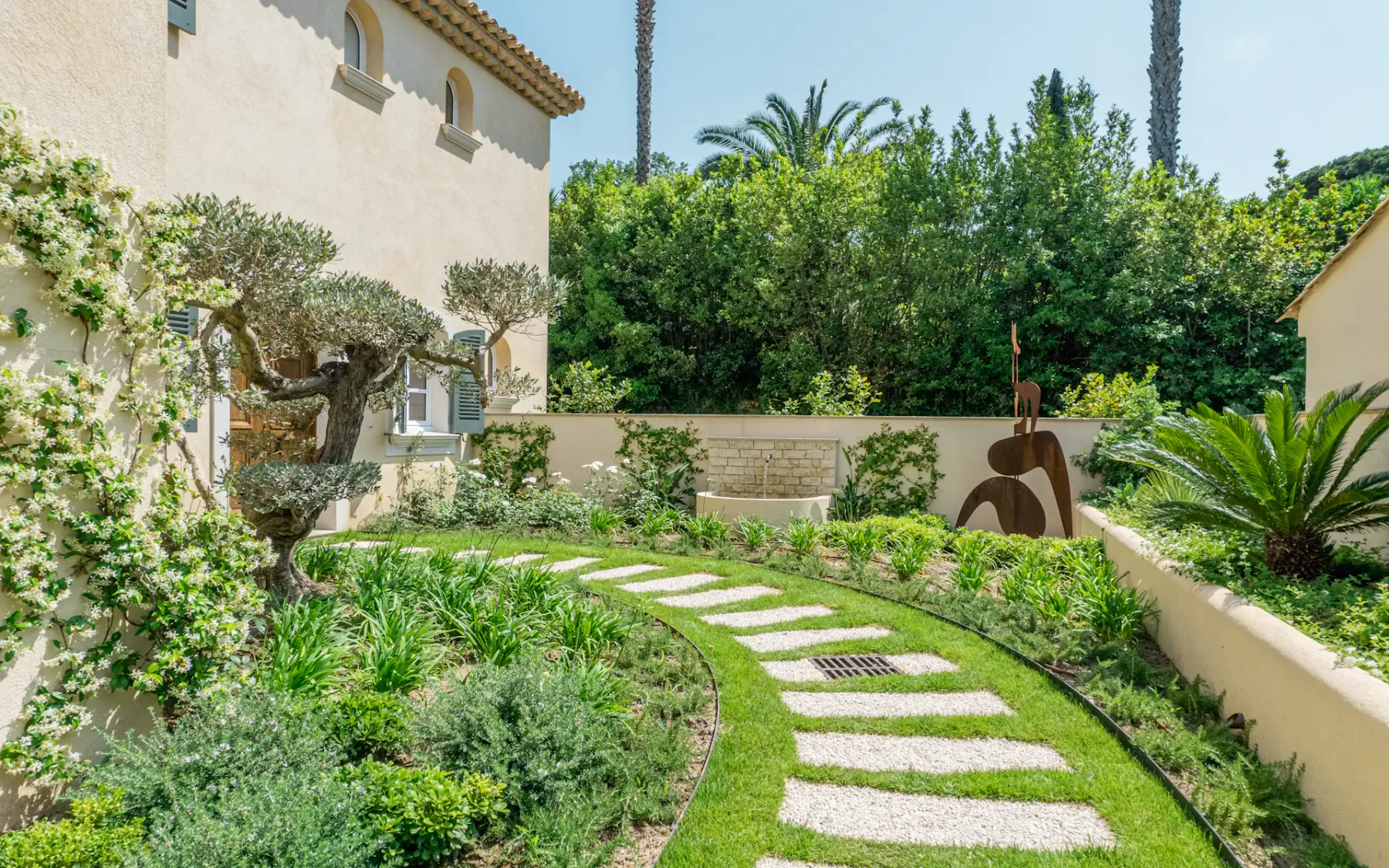 Un sendero ajardinado se curva entre la vegetación junto a una casa de estuco.