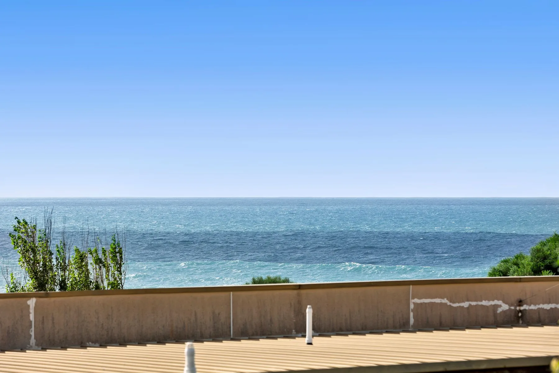 A seaside terrace overlooks the ocean beneath a clear blue sky.