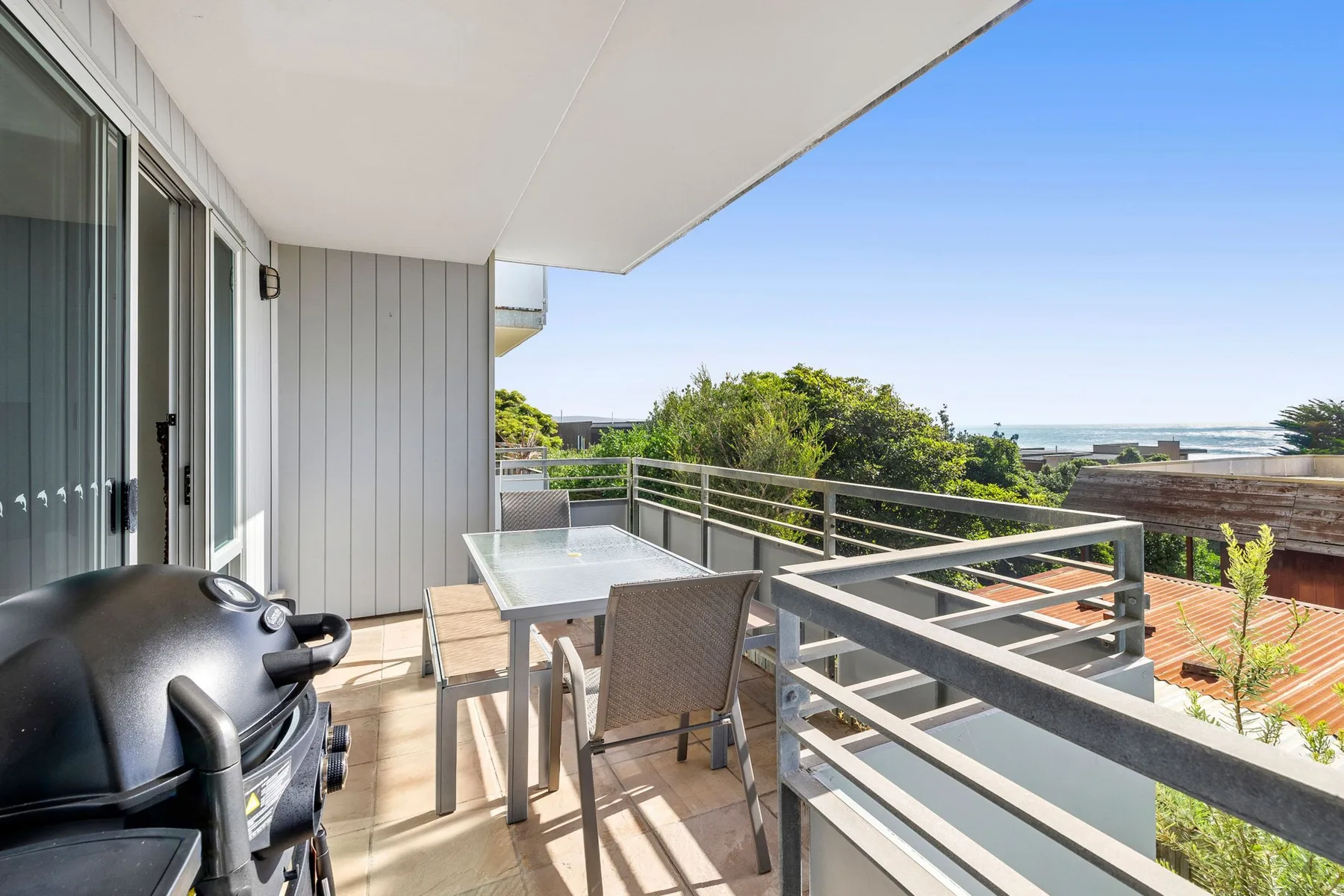 A balcony dining area with a table, seating, and a view of greenery.