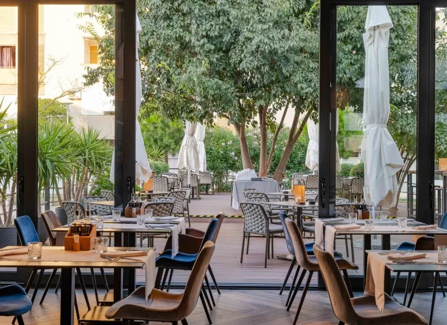 Espacio representativo del hotel: Una zona de comedor con mesas y asientos se abre a un patio exterior frondoso.