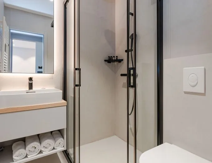 Espacio representativo del hotel: Un baño moderno con lavabo, espejo y ducha de vidrio.