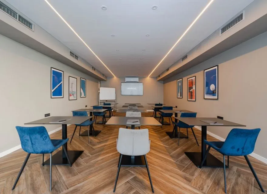 Espacio representativo del hotel: Una sala de reuniones con filas de mesas, sillas y cuadros enmarcados.
