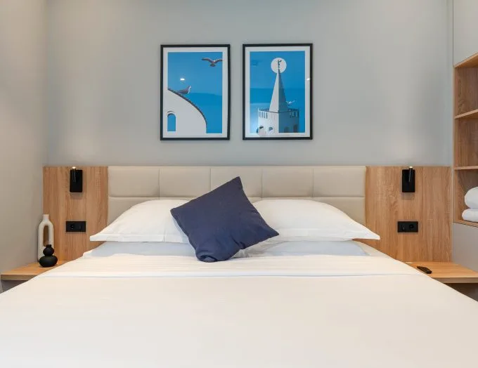 Espacio representativo del hotel: Una cama de hotel bien tendida está debajo de dos cuadros enmarcados.