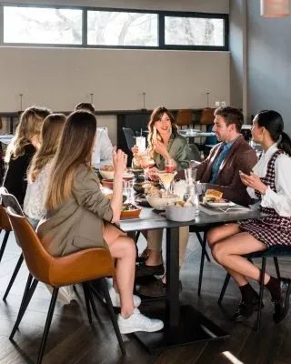 Espacio representativo del hotel: Varias personas se reúnen alrededor de una mesa para comer en un comedor luminoso.