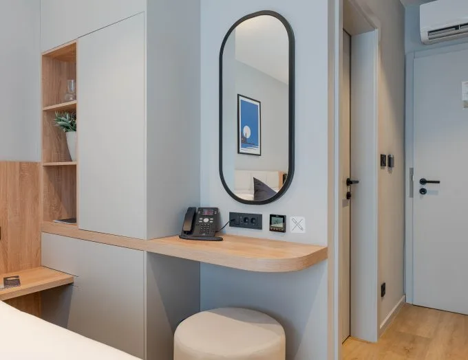 Espacio representativo del hotel: Un tocador de habitación de hotel con un espejo ovalado y un taburete pequeño.