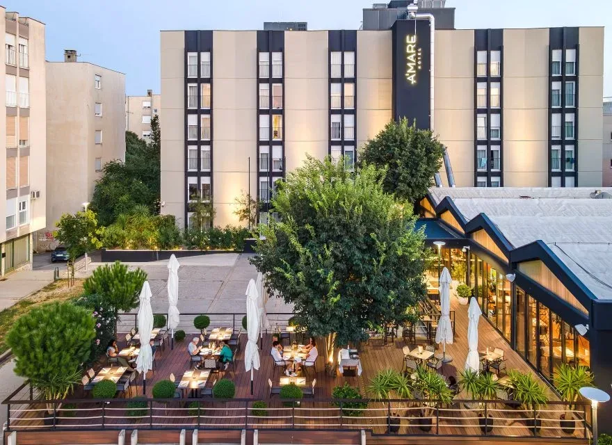 Espacio representativo del hotel: Patio del hotel con asientos al aire libre y árboles frente al edificio principal.