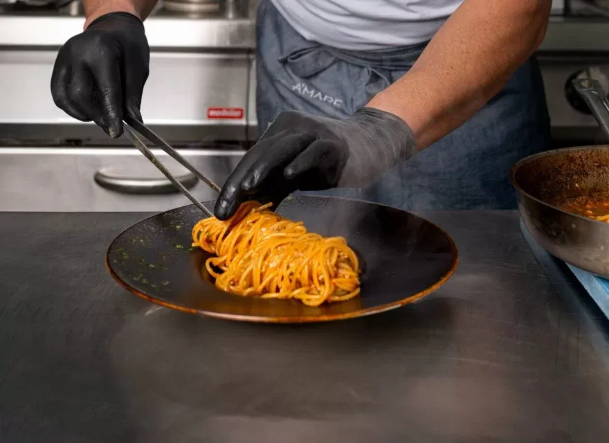 Espacio representativo del hotel: Un cocinero sirve pasta sobre una superficie de trabajo de acero inoxidable.
