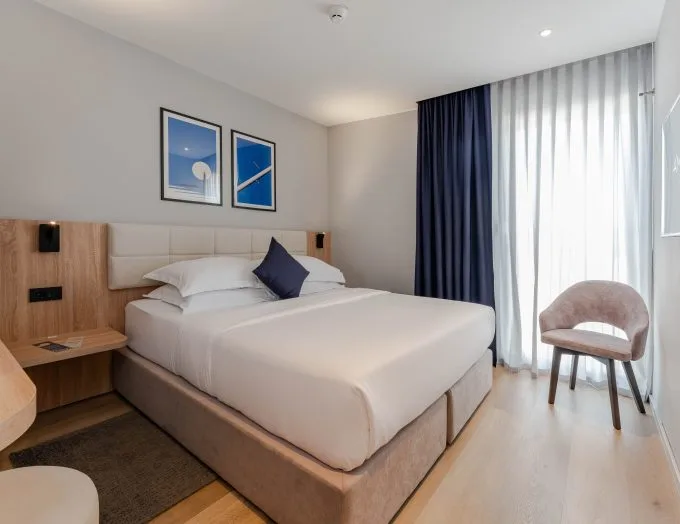 Espacio representativo del hotel: Un dormitorio con una cama bien tendida junto a una ventana luminosa.