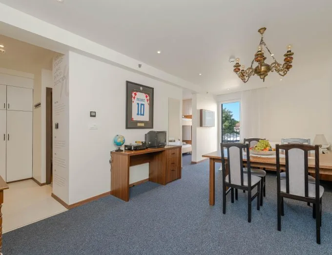 Espacio representativo del hotel: Un comedor con mesa y sillas está junto a un escritorio y una camiseta deportiva enmarcada.