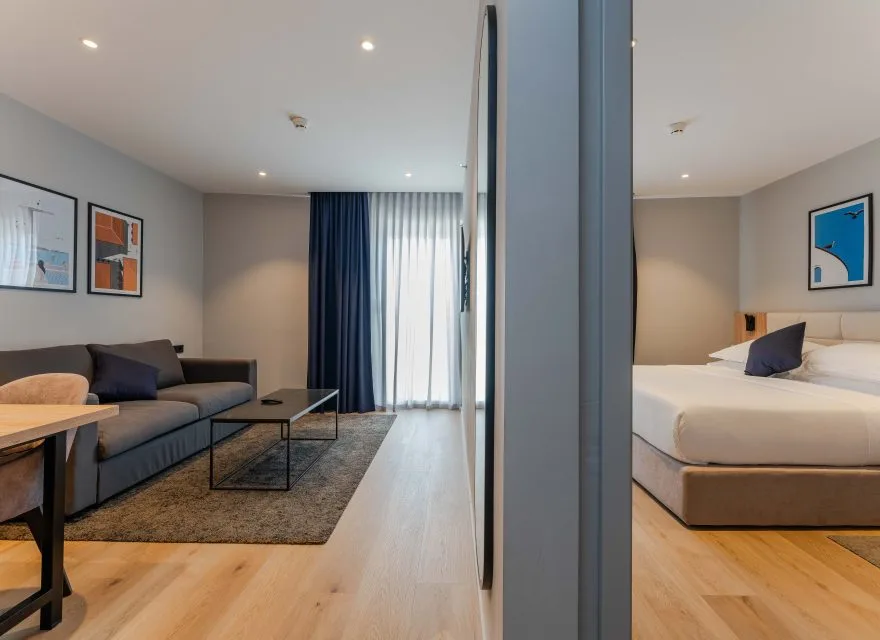 Espacio representativo del hotel: Una habitación de hotel combina una zona de estar con una cama junto a cortinas de suelo a techo.