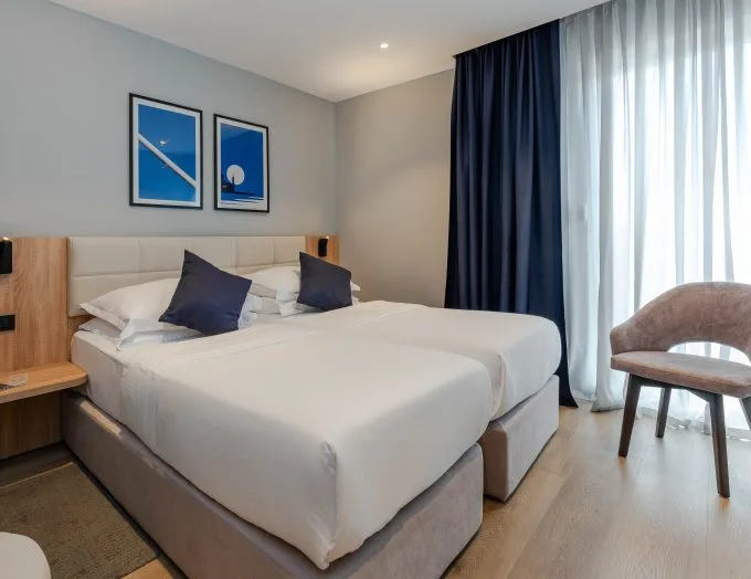 Espacio representativo del hotel: Un dormitorio de hotel con dos camas, cuadros enmarcados y una silla junto a la ventana.