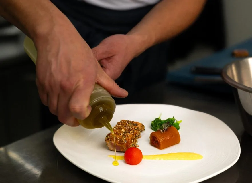 Espacio representativo del hotel: Una persona añade salsa a un plato servido en una cocina.