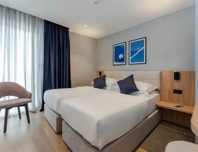 Espacio representativo del hotel: Un dormitorio con una cama tendida, cuadros enmarcados y cortinas junto a la ventana.