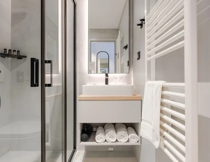 Espacio representativo del hotel: Baño luminoso con lavabo, espejo y ducha de vidrio.