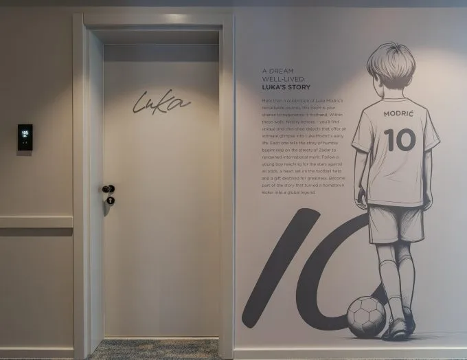 Espacio representativo del hotel: Un pasillo tiene una puerta junto a una gran ilustración mural de fútbol.