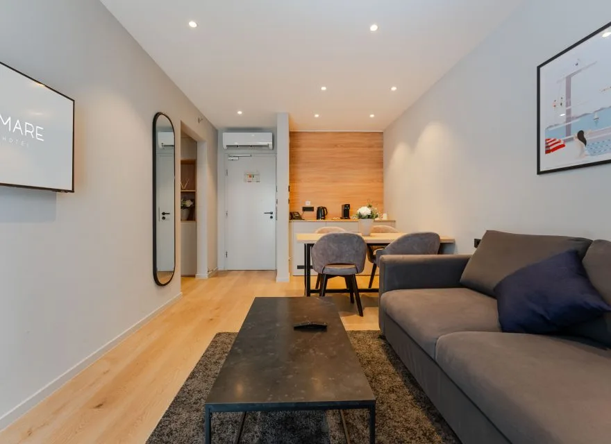 Espacio representativo del hotel: Una sala de estar con asientos y una mesa de centro da a una cocina compacta.