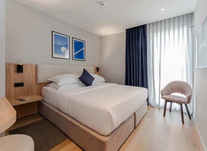 Espacio representativo del hotel: Un dormitorio con una cama tendida, cuadros enmarcados y cortinas junto a la ventana.