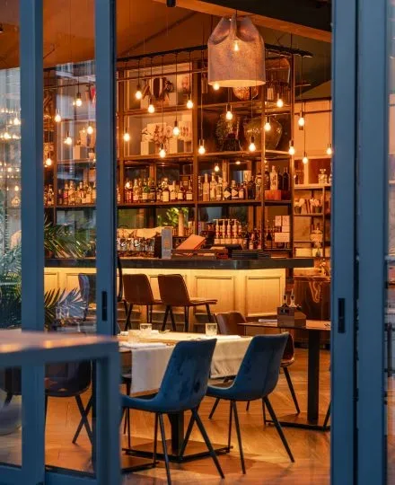Espacio representativo del hotel: Una zona de bar y comedor iluminada con calidez, con botellas en estantes tras la barra.