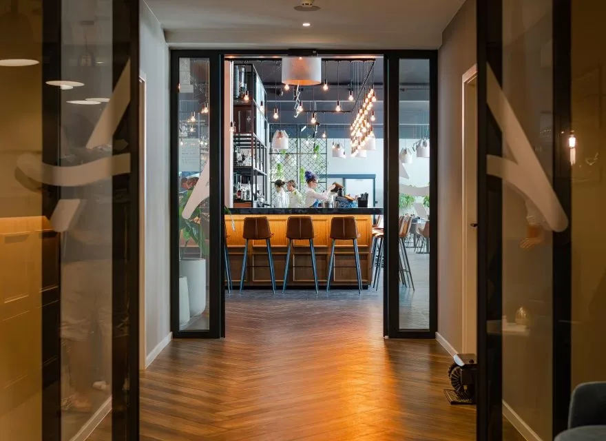 Espacio representativo del hotel: Un pasillo da a una zona de bar con taburetes y lámparas colgantes.
