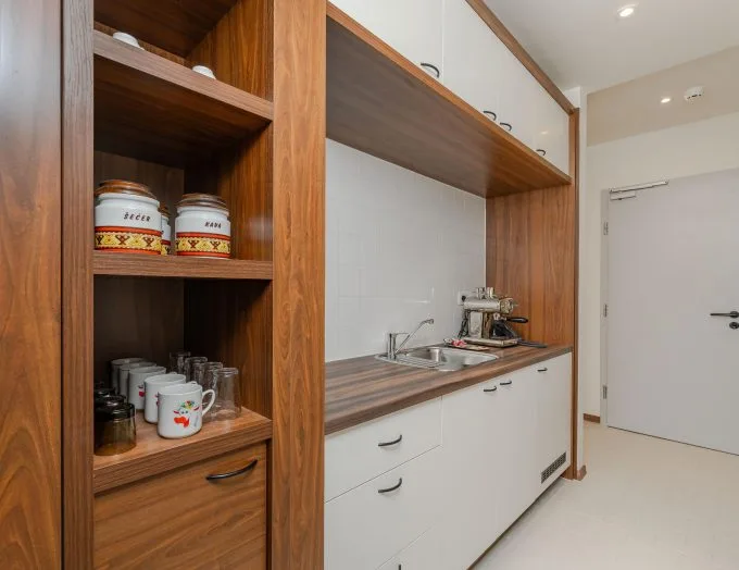 Espacio representativo del hotel: Una pequeña cocina con estantes de madera, armarios blancos y un fregadero.