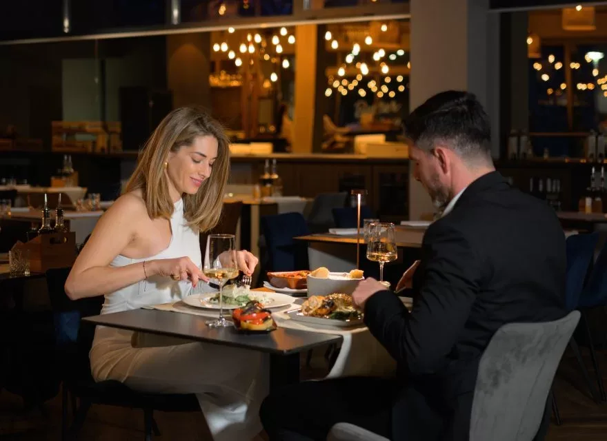 Espacio representativo del hotel: Una pareja cena en una mesa de restaurante bajo luces cálidas colgantes.