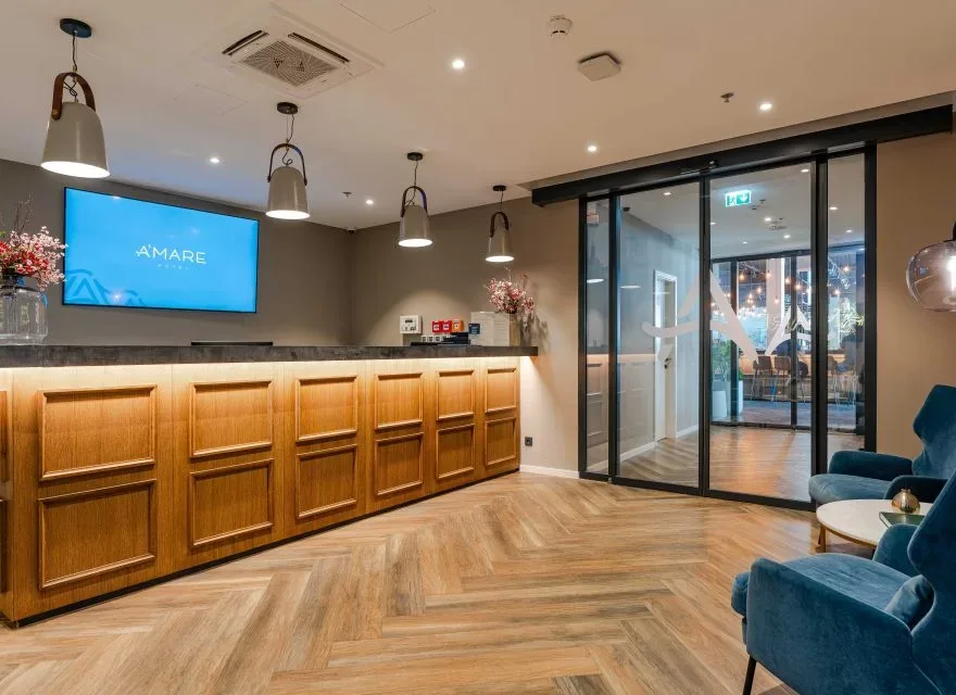 Espacio representativo del hotel: Una recepción de hotel con un mostrador de madera y puertas de vidrio.