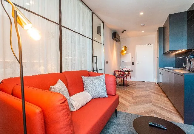 Una luminosa sala de estar con asientos rojos junto a una cocina compacta.