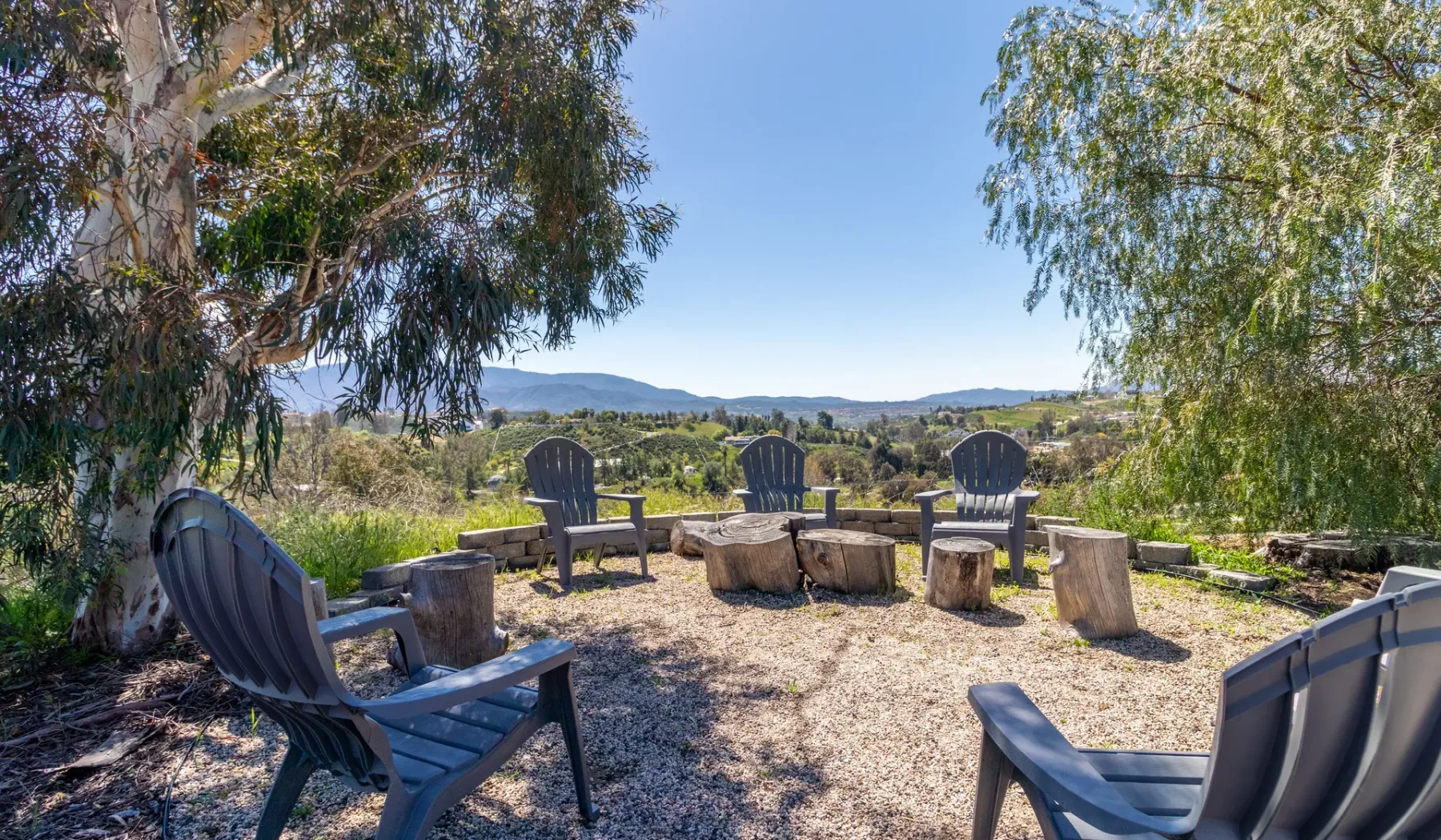 Outdoor seating area with chairs arranged beneath trees, overlooking a wide landscape.