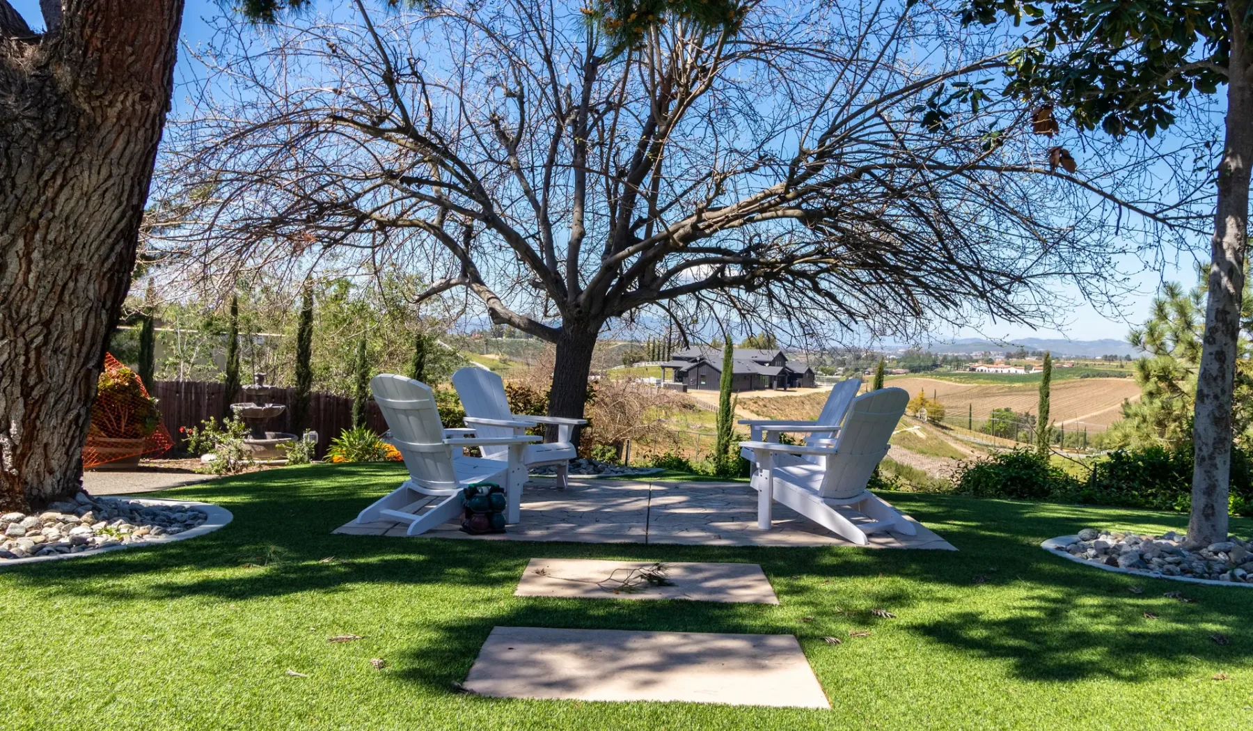 A shaded lawn seating area beneath a large tree overlooks open fields.