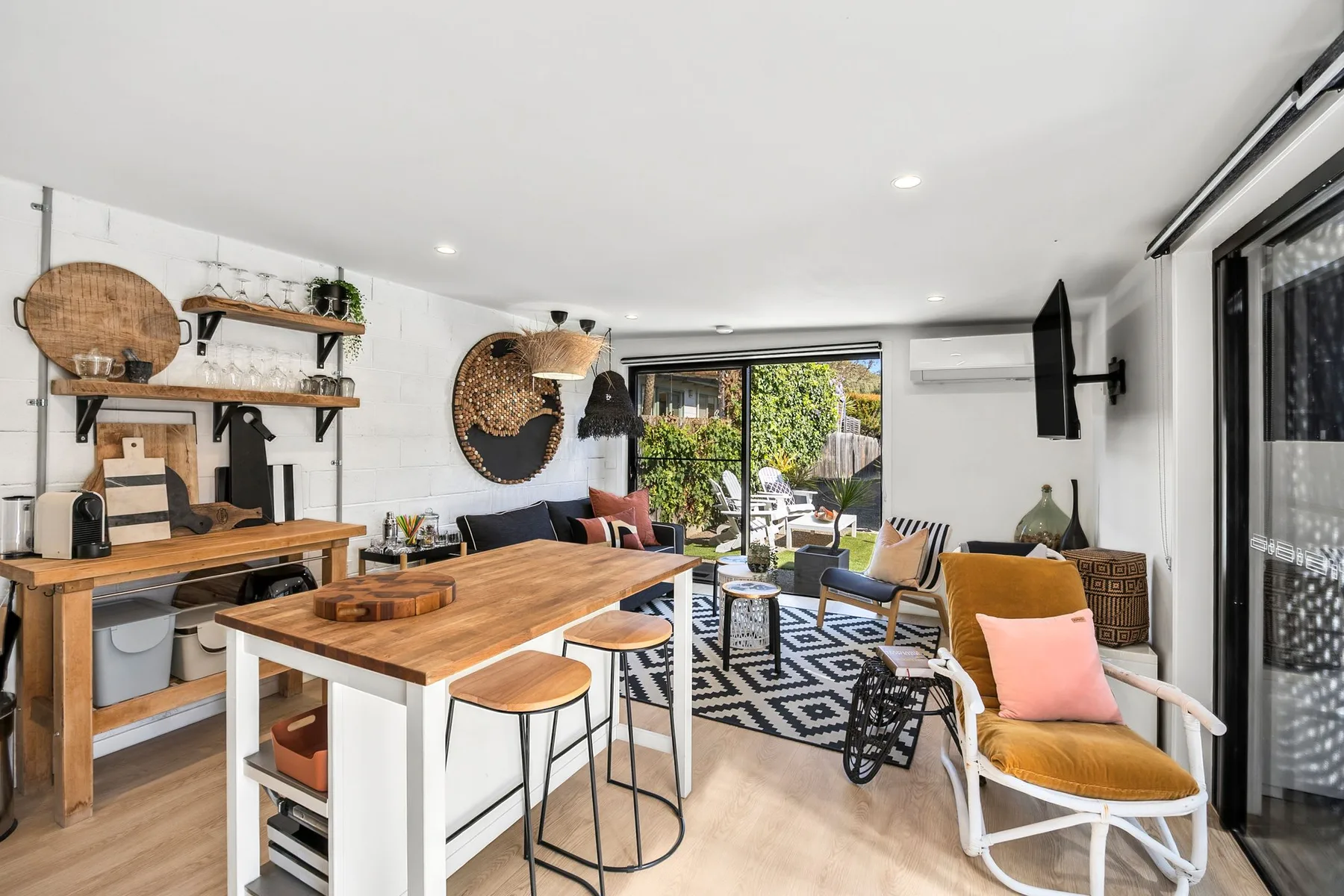 Una zona abierta de estar y comedor tiene una mesa de madera y asientos junto a puertas de vidrio.