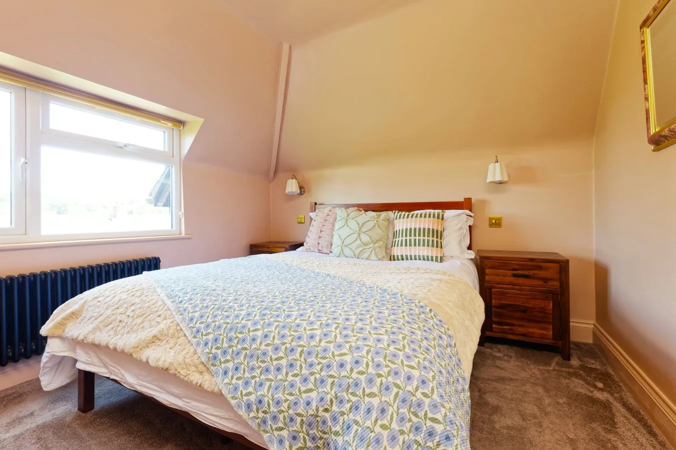 A bedroom with a bed dressed in patterned bedding beside a large window.