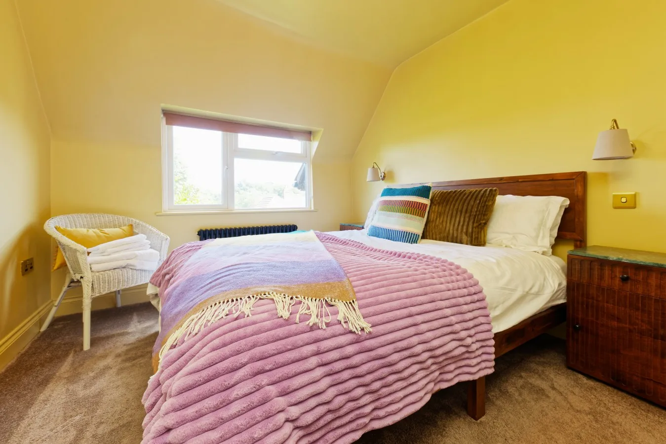A bedroom with a bed covered in a pink quilt beside a window.
