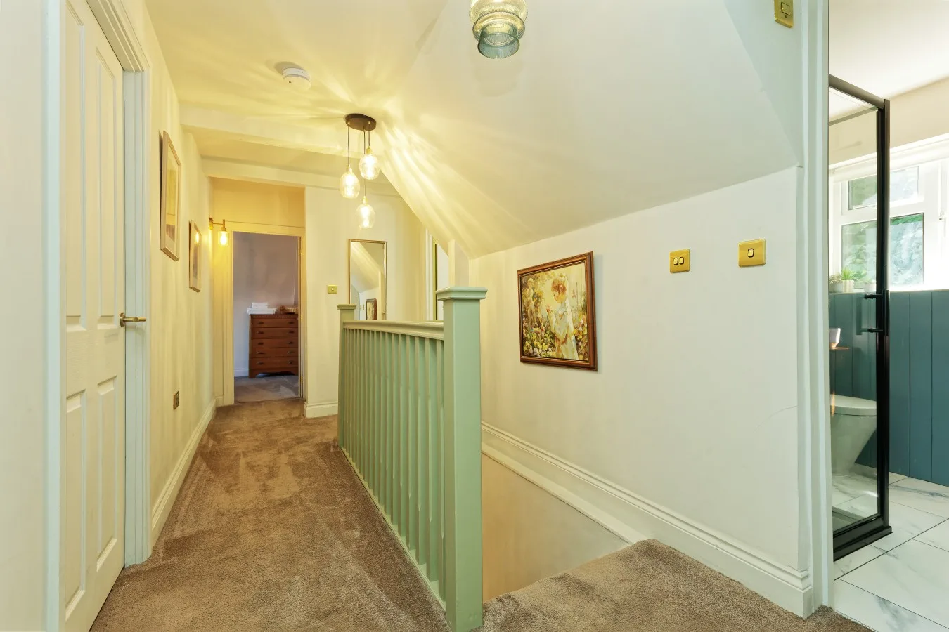 A carpeted hallway with a painted railing and framed artwork on the wall.