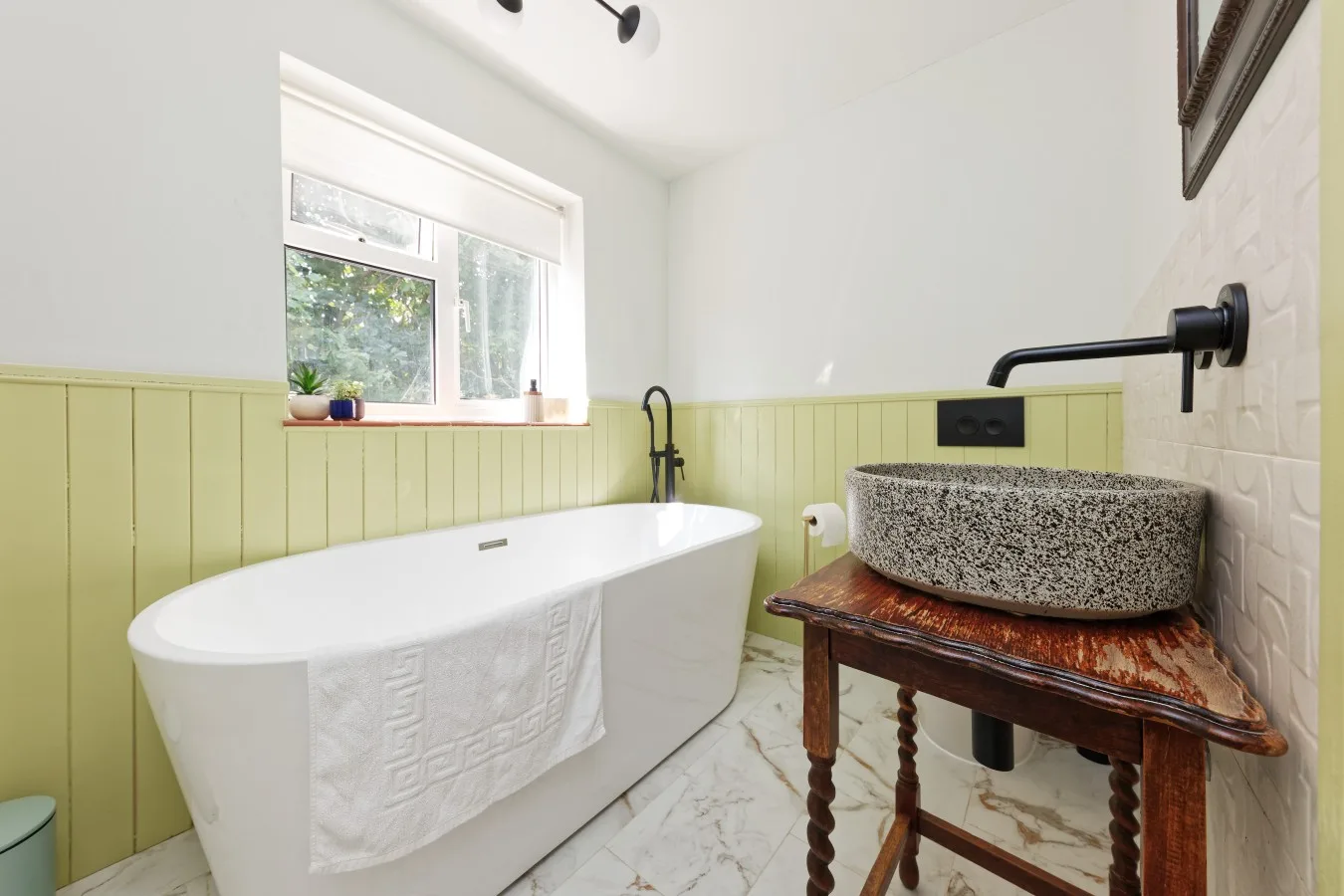 A bright bathroom with a freestanding bathtub and a stone vessel sink.