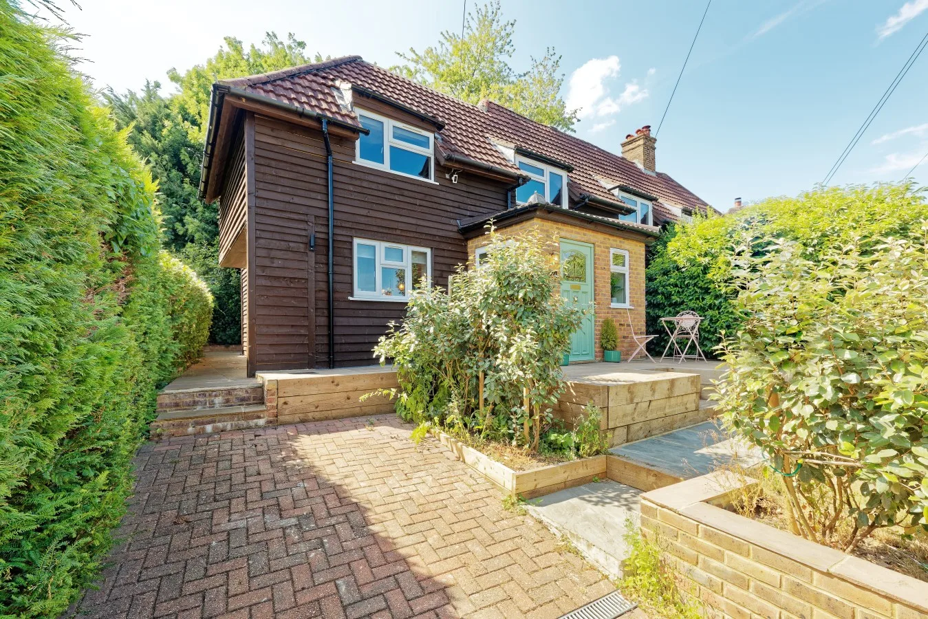 A two-story house with a brick-paved path and leafy garden.
