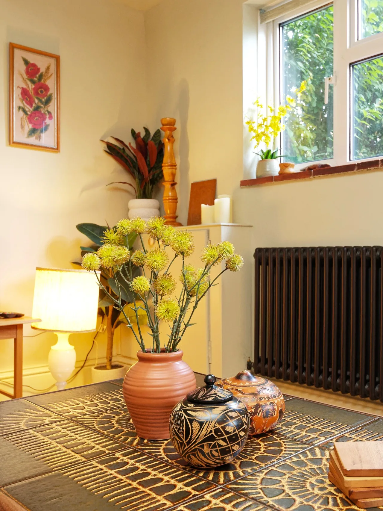 A warmly lit living room has a patterned table with flowers and decorative vessels.