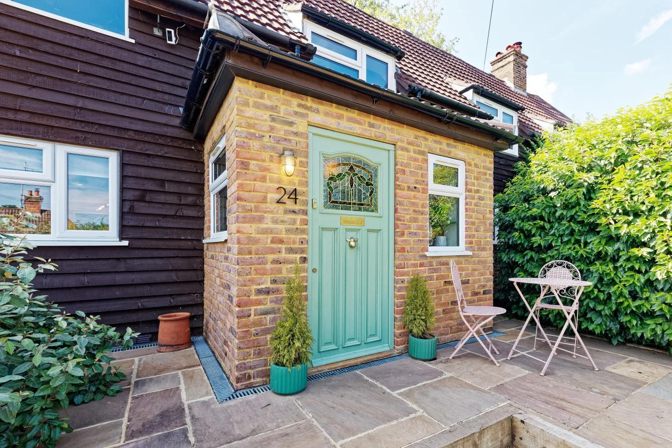 A brick entrance with a green door opens onto a paved patio.