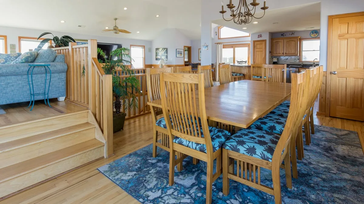 Comedor con una mesa larga de madera y asientos estampados, junto a una sala de estar.