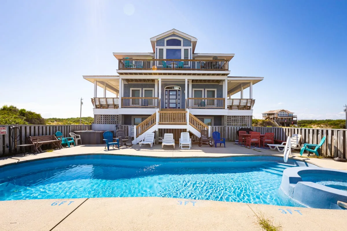A large multi-level house stands behind a swimming pool and outdoor seating.