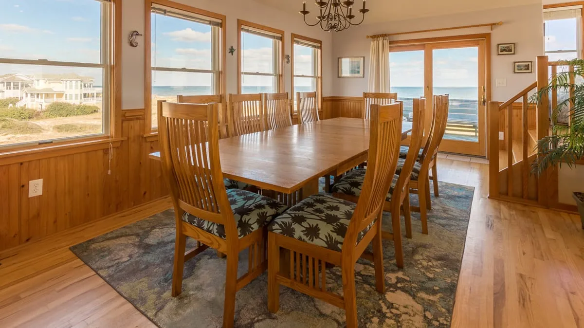 Un comedor con una mesa de madera y grandes ventanas con vistas al agua.