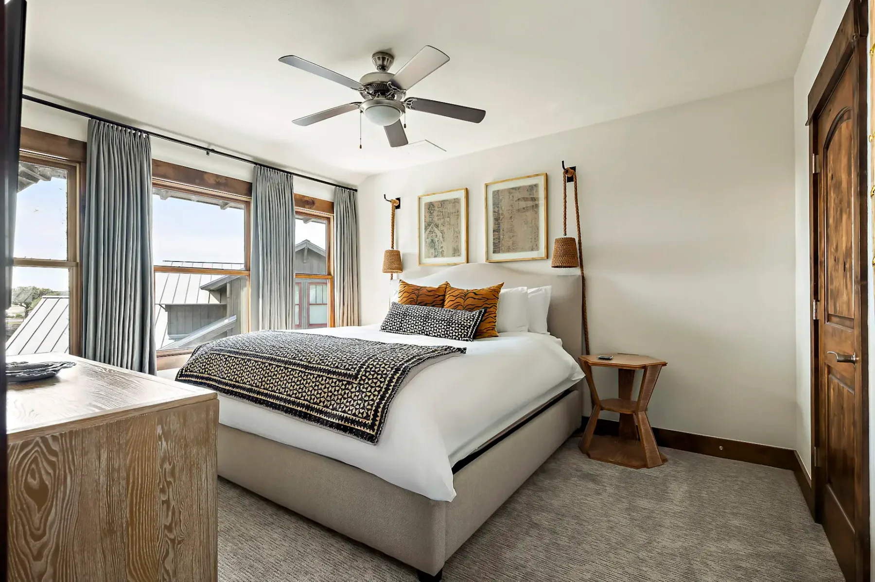 Un dormitorio con una cama, ropa de cama estampada y ventanas con cortinas.