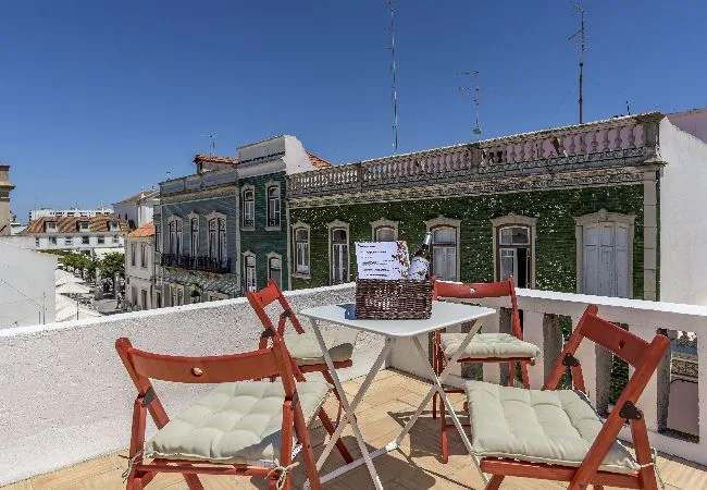 A rooftop terrace has red folding chairs and a table overlooking nearby buildings.