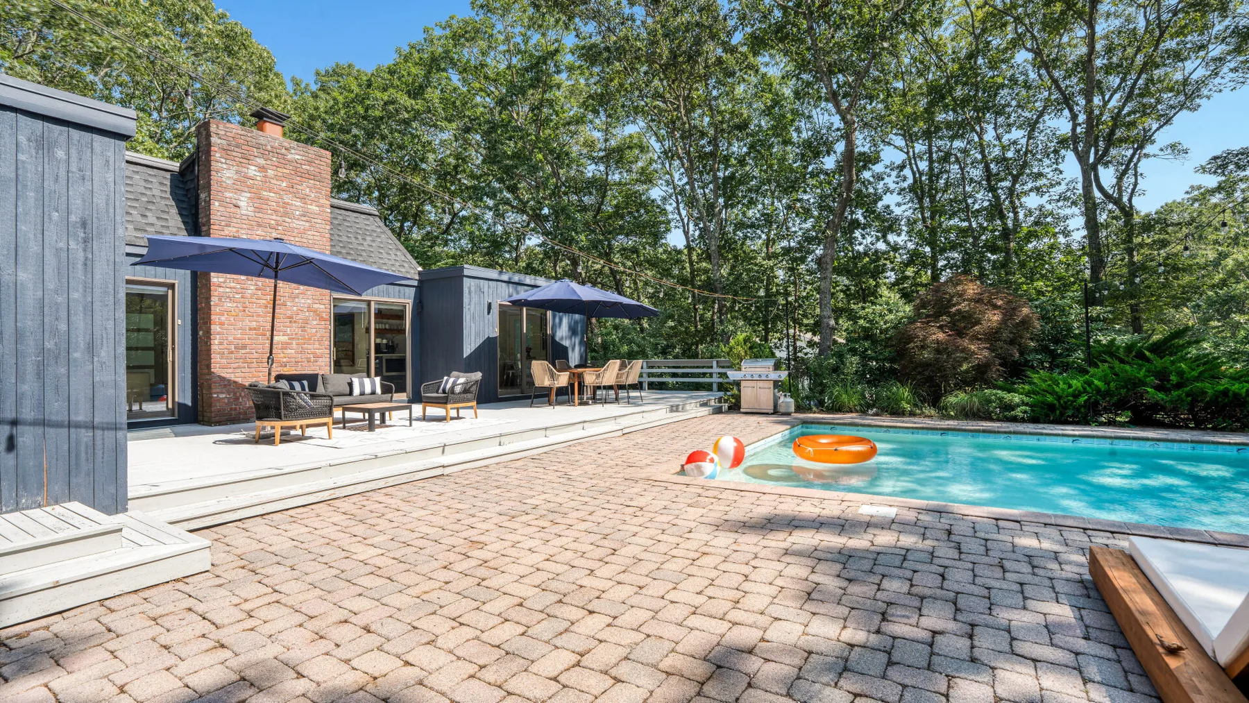 Un patio trasero junto a una piscina, con asientos al aire libre y sombrillas.