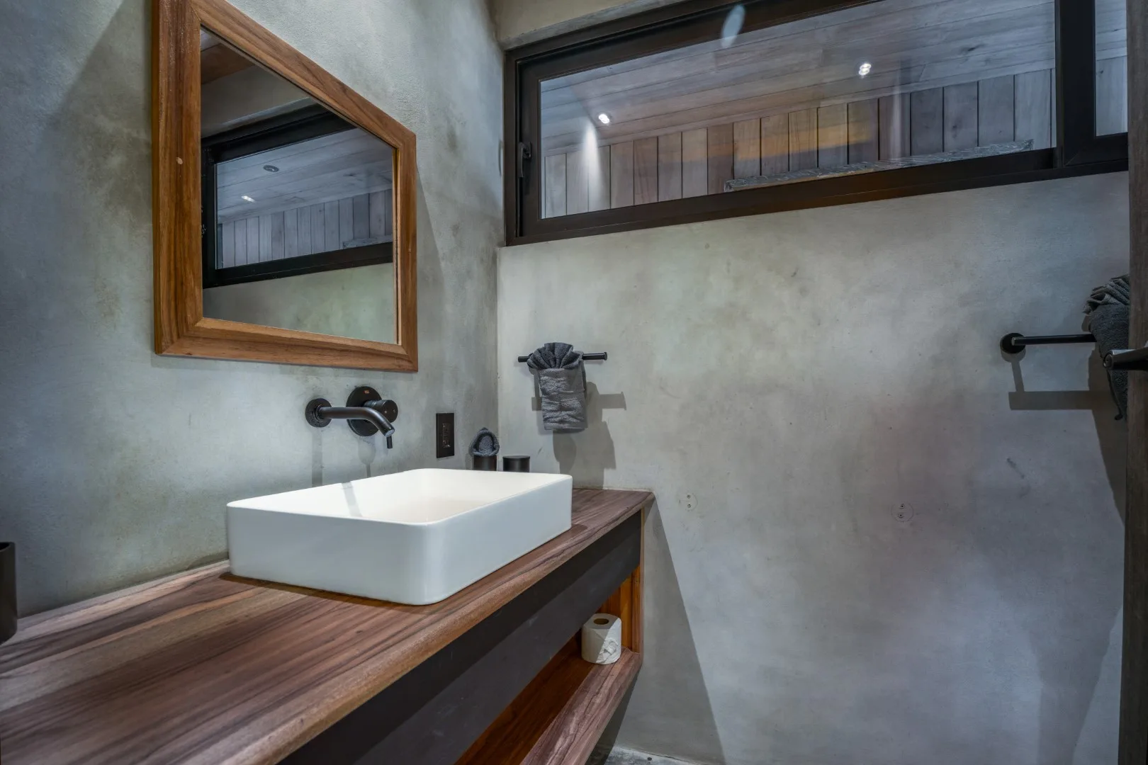Un baño moderno tiene un lavabo blanco sobre encimera bajo un espejo con marco de madera.