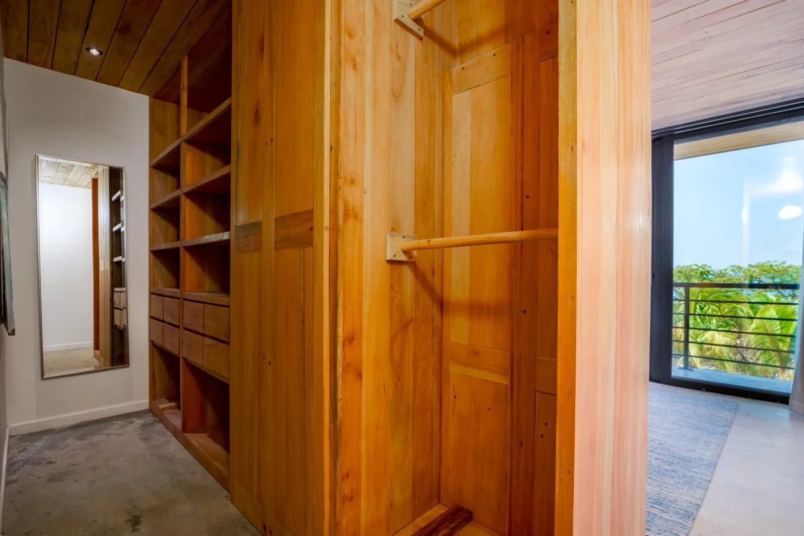 Un área de armario revestida de madera con estantes abiertos junto a una habitación luminosa.