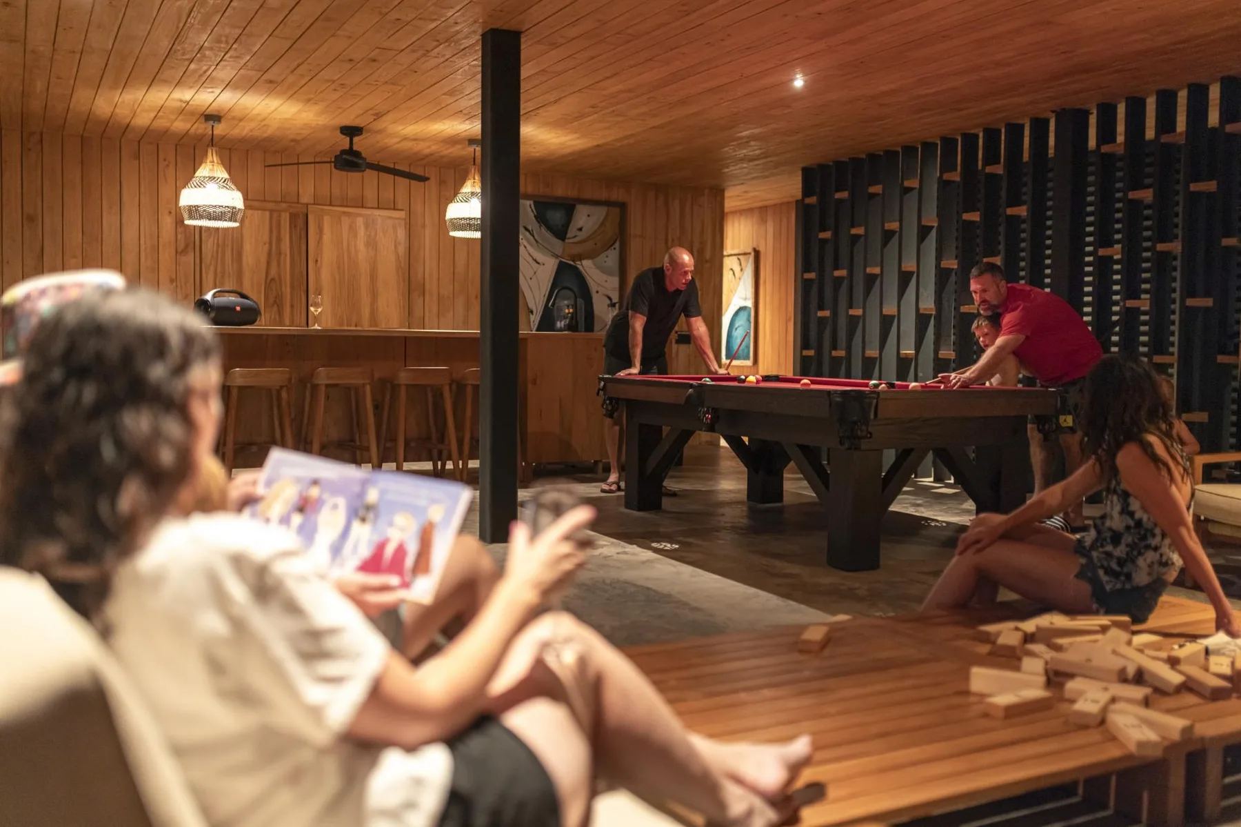Una sala de juegos revestida de madera, con personas jugando al billar y descansando cerca.
